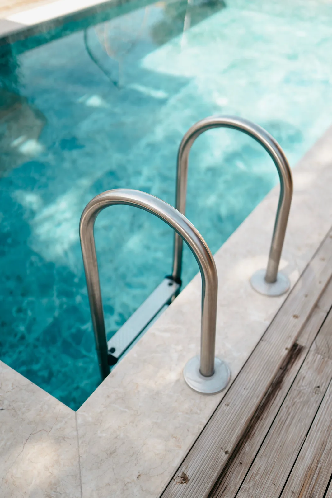 Stainless steel pool ladder and handrails entering clear blue pool water, representative of a residential pool in the Reno/Sparks area